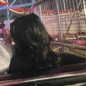 two people sitting on a bench in front of a carnival ride at night, one is talking on the phone