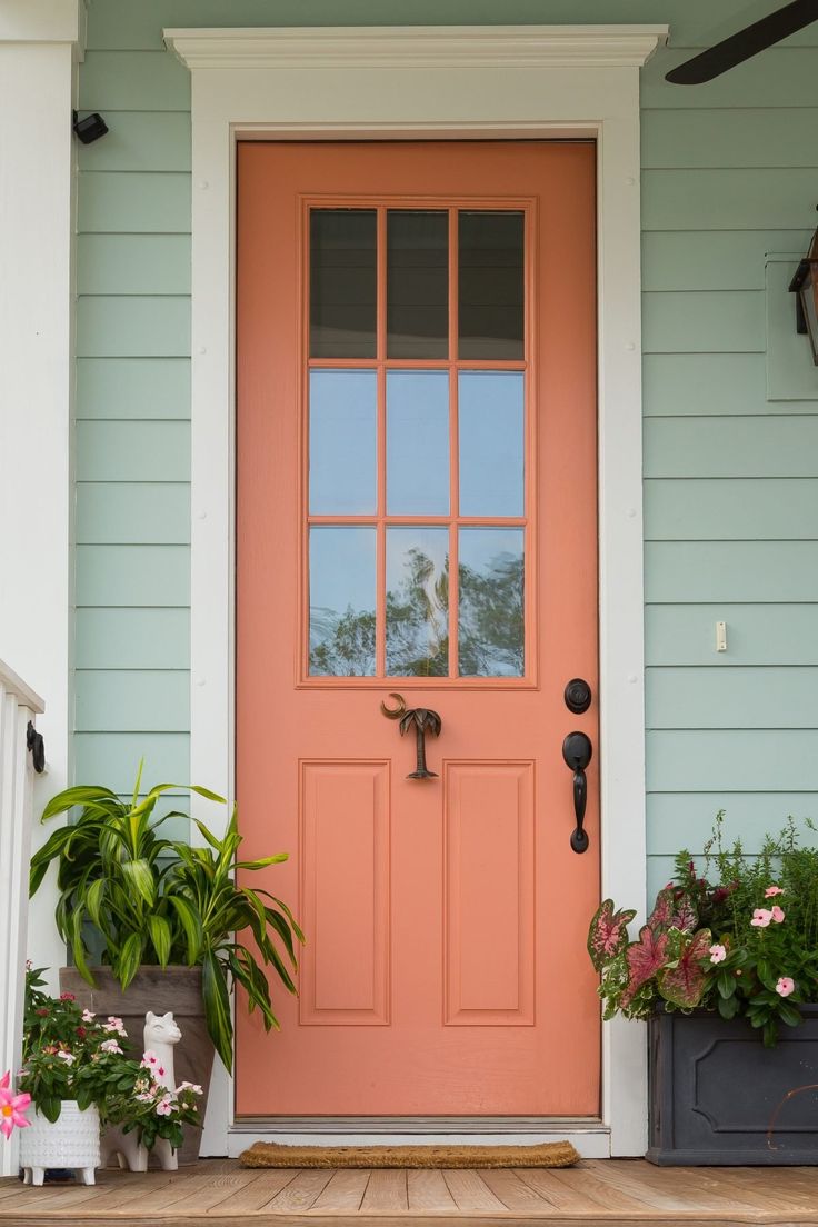 an orange front door with potted plants on the porch