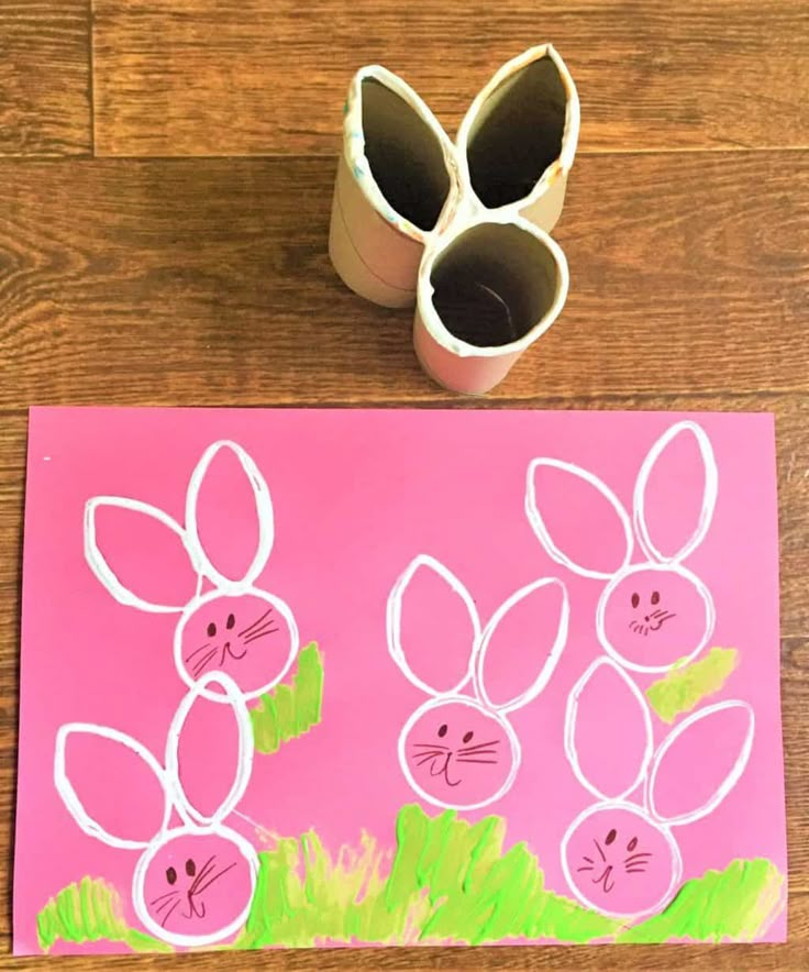 toilet paper roll bunny stamps on a pink background next to a cup with rolled up easter eggs