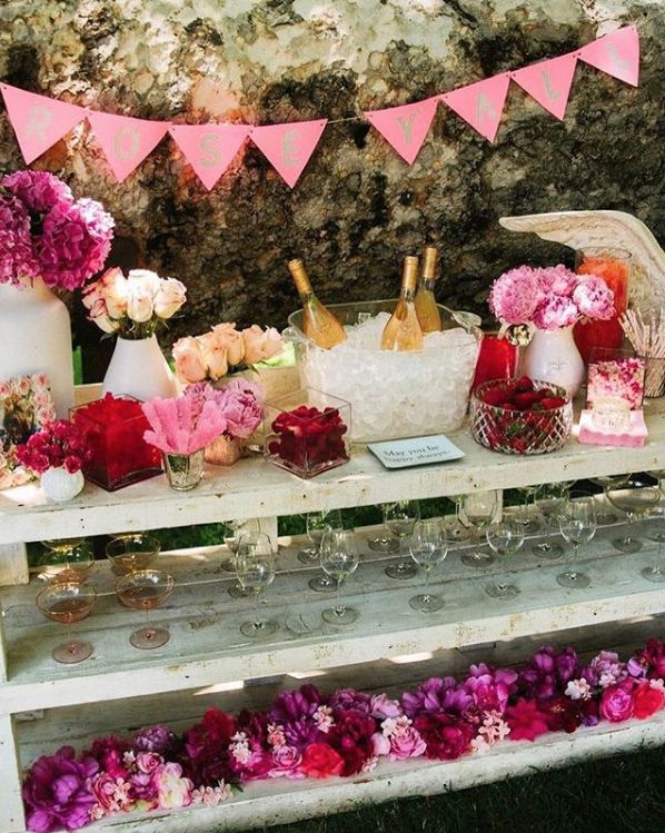 the table is covered with pink and white flowers, wine bottles, and desserts