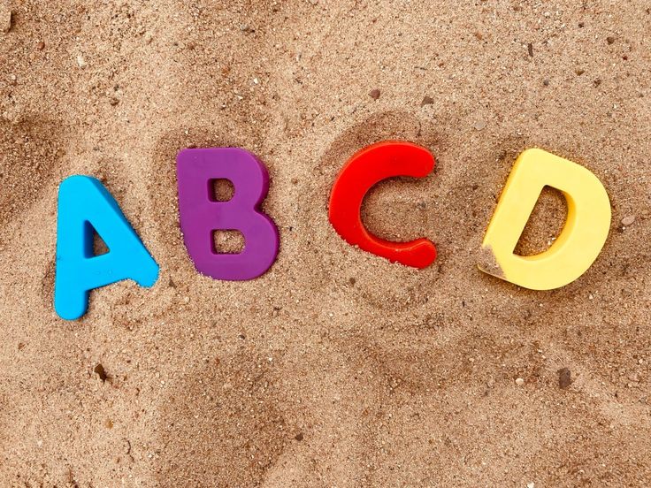 the word abcd spelled with colorful plastic letters in the sand