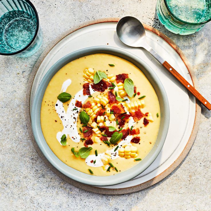 a bowl of soup with bacon, corn and cheese on the side next to two glasses