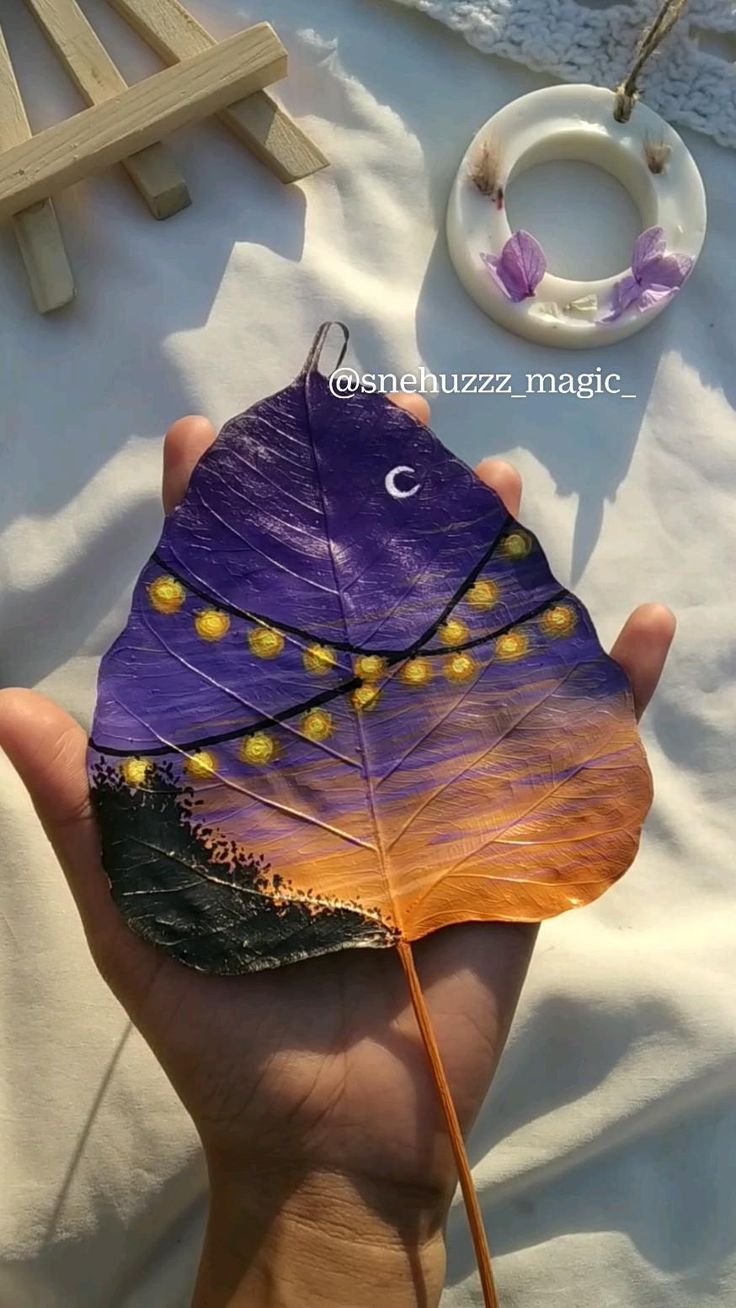 a hand holding a purple leaf with yellow dots on it and a white necklace hanging from the end