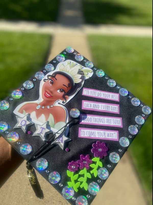 a hand holding a decorated graduation cap with an image of princess and the frog on it