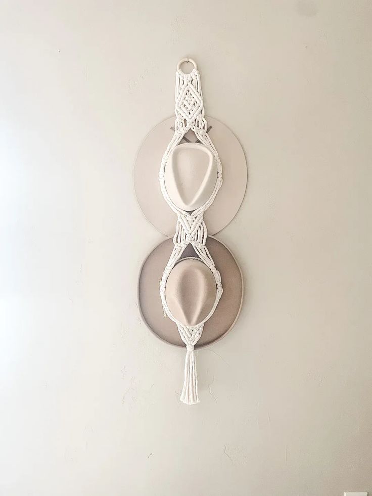 a white wall clock hanging from the side of a wall next to a plate with a tassel on it