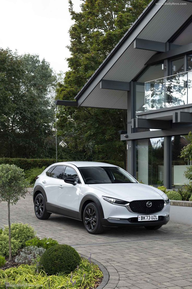 a white mazda cx - 30 parked in front of a modern house with large windows