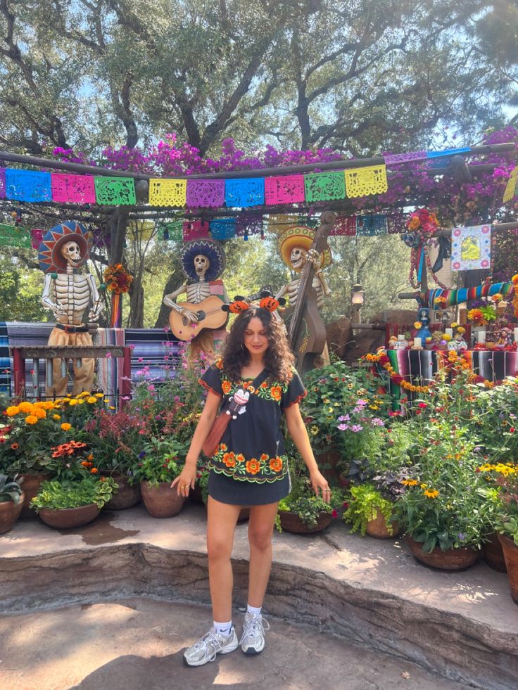 a woman standing in front of a display of flowers and skeleton statues at a mexican themed park