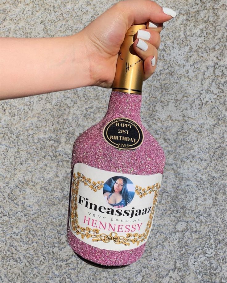 a hand holding a pink bottle with a gold cap