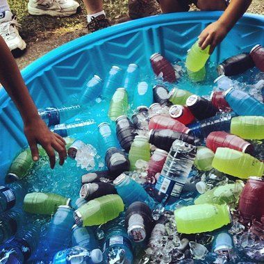 several people in a blue tub filled with water and plastic soda bottles, one holding a green bottle