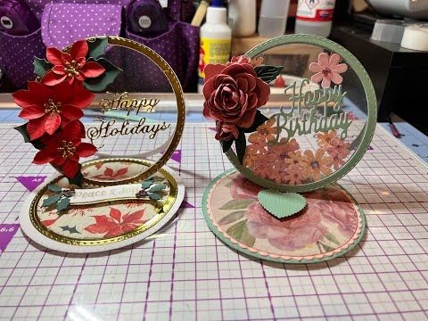 two cards with flowers on them sitting on a table next to scissors and other crafting supplies