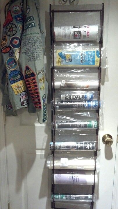 an over the door magazine rack holds magazines and other items in plastic wrap, along with t - shirts on hangers