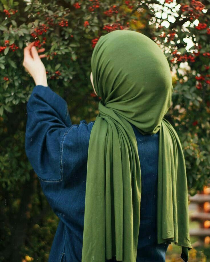 a woman wearing a green shawl standing in front of a tree with red berries on it