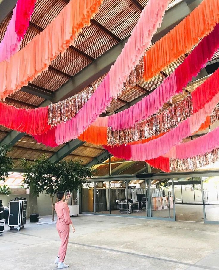 there is a woman that is walking under some pink and orange streamers hanging from the ceiling