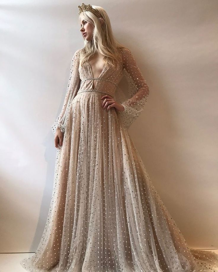 a woman in a long dress standing next to a white wall wearing a tiara