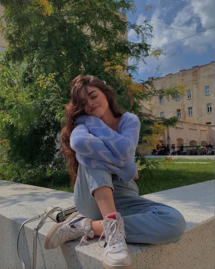 a young woman sitting on the edge of a cement wall with her hands behind her head