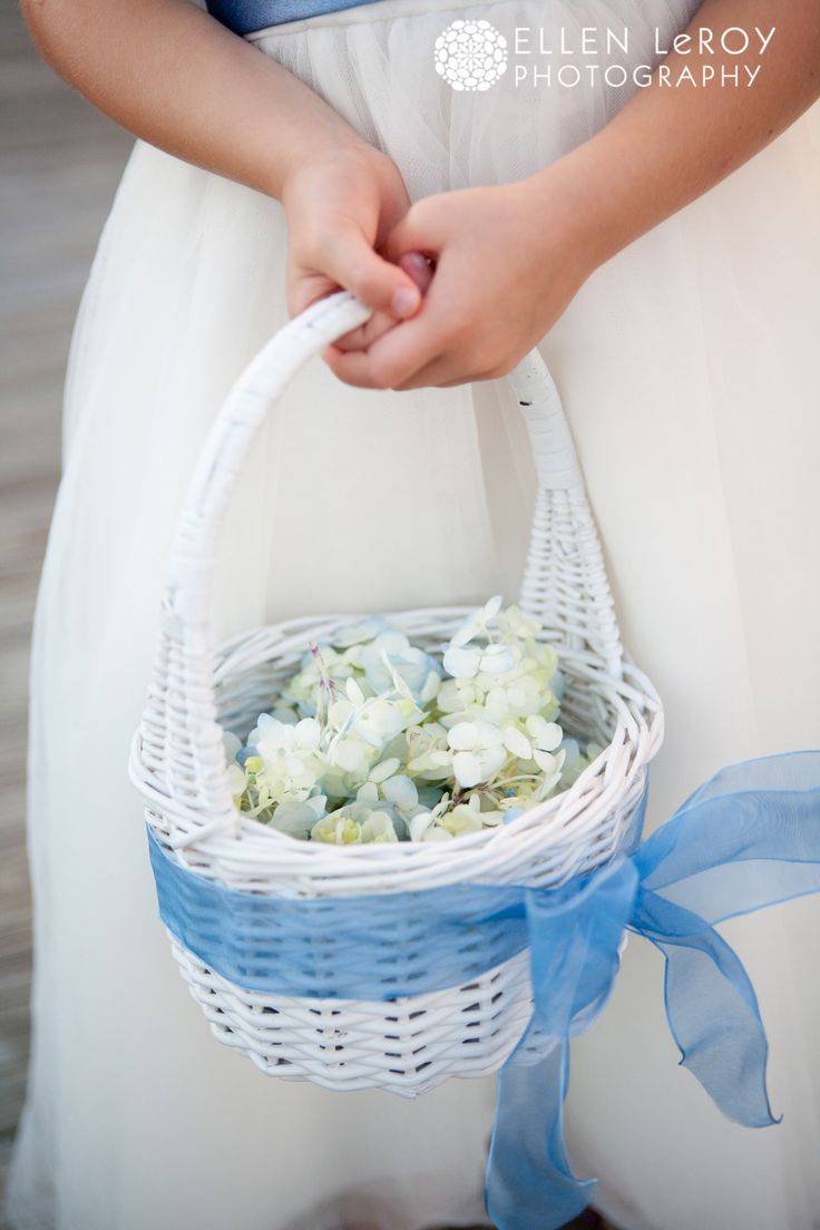 a woman in a white dress holding a basket with flowers on the inside and blue ribbon