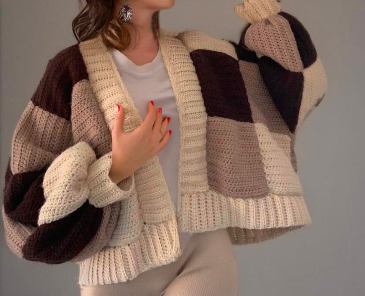 a woman is wearing a knitted sweater and holding her hand up to her face