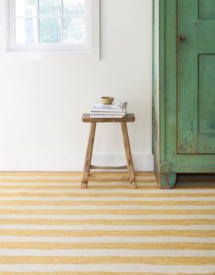 a green cabinet sitting next to a yellow and white striped rug on top of a wooden table