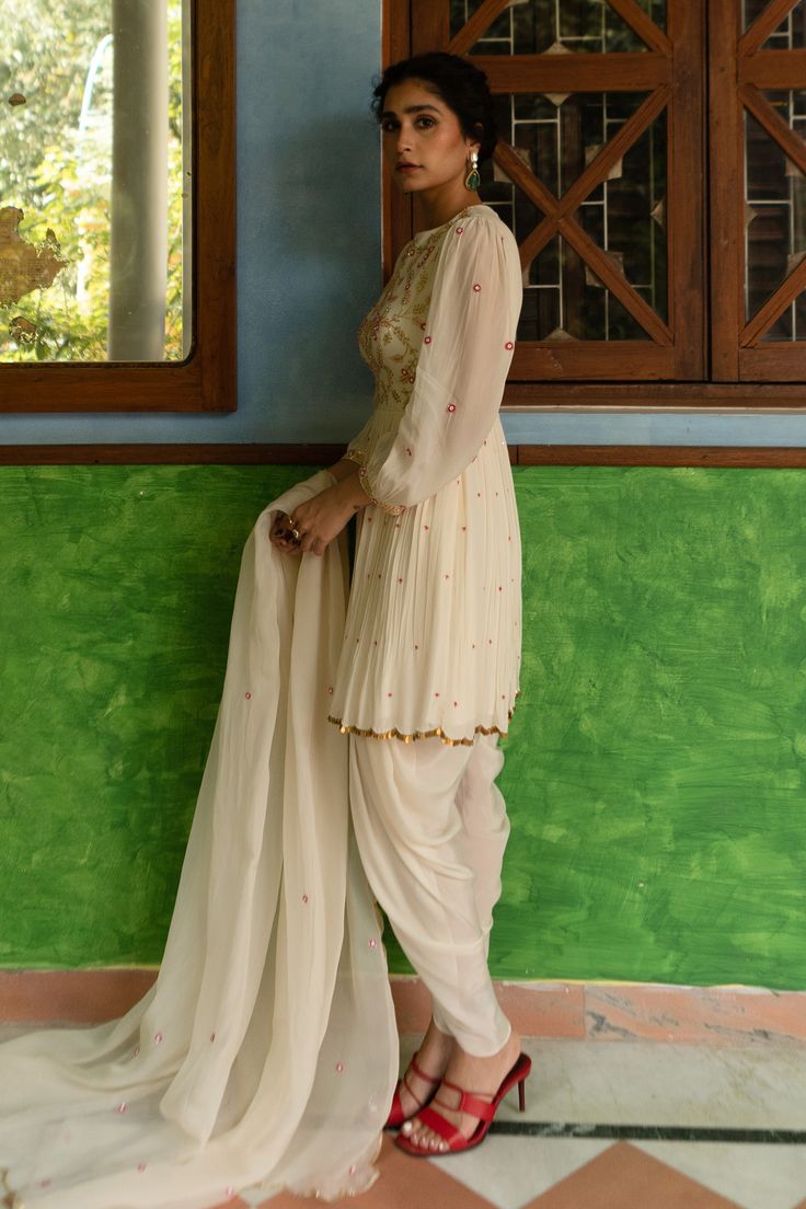 Off white balloon sleeve kurta, highlighted with flower embroidery in cutdana poth tikki jaal work. Paired with a dhoti pant and dupatta.
Components: 3
Pattern: Embroidery
Type Of Work: Cutdana Poth Tikki Jaal
Neckline: Round Neck
Sleeve Type: Balloon Sleeves
Fabric: Kurta and Dhoti Pant: Pure Crepe, Dupatta: Viscose Organza
Color: Off White
Other Details: 
Pleated and scallop trim kurta
Scallop trim dupatta with butti embroidery
Draped dhoti pant
Occasion: Sangeet - Aza Fashions Butti Embroidery, New Dress Pattern, Kurta Patterns, Dhoti Pants, White Kurta, White Peplum, Scallop Trim, Pattern Embroidery, Flower Embroidery