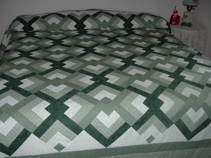 a bed with a green and white quilt on it's headboard next to a night stand