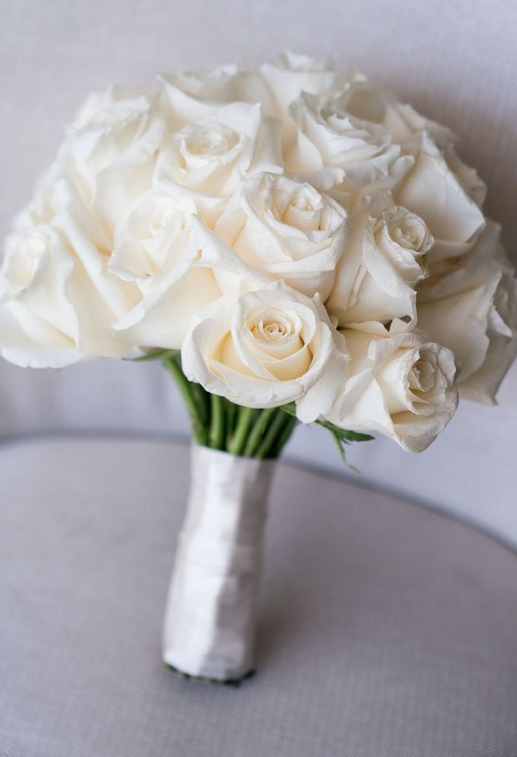 a bouquet of white roses sitting on top of a table in front of a chair