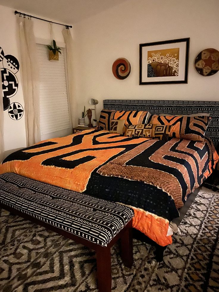 a bed with an orange and black comforter on top of it next to a window