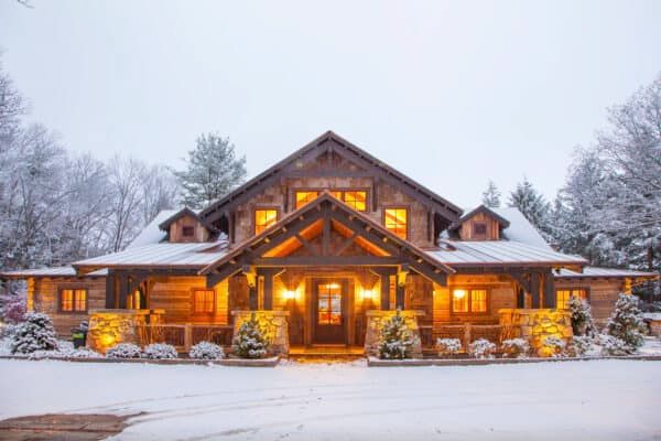 a large log home in the snow with lights on it's front door and windows