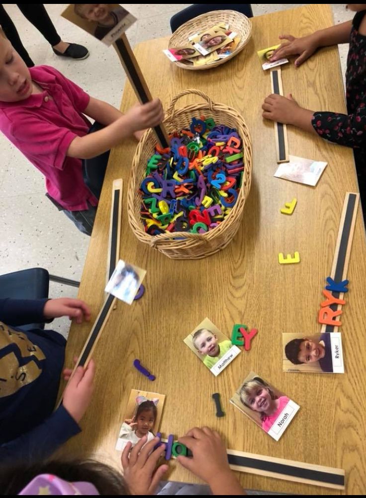 children are sitting at a table playing with letters and magnets on the table in front of them