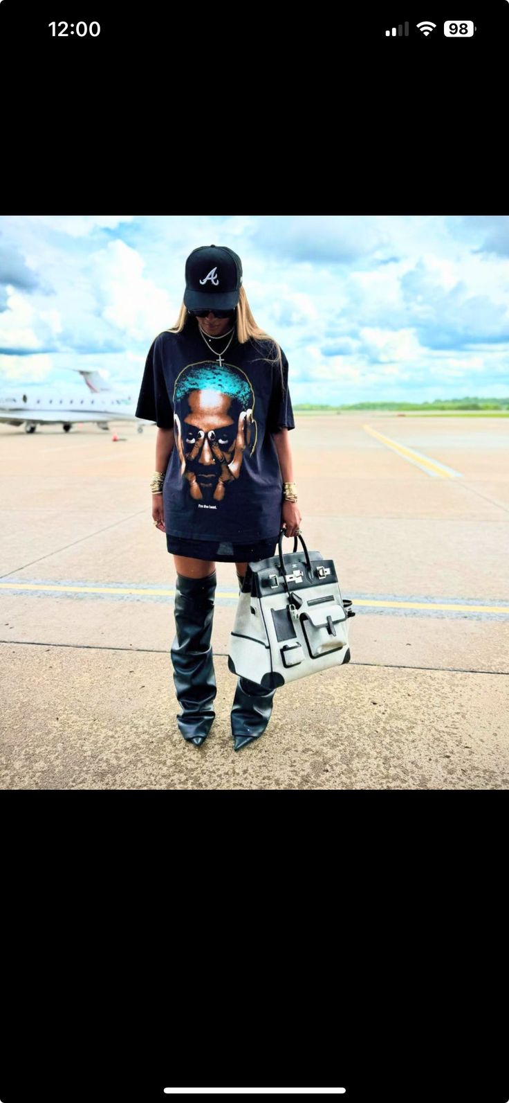 a person standing on top of an airport tarmac holding a handbag and wearing knee high boots