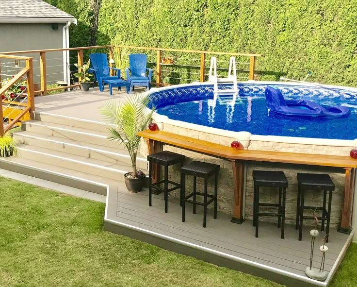 an above ground swimming pool surrounded by grass and wooden decking with bar stools