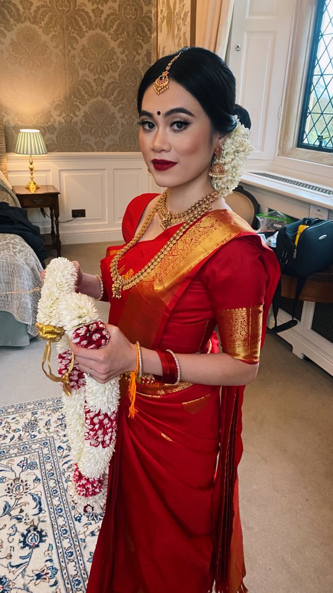 a woman in a red and gold sari holding a white vase with flowers on it