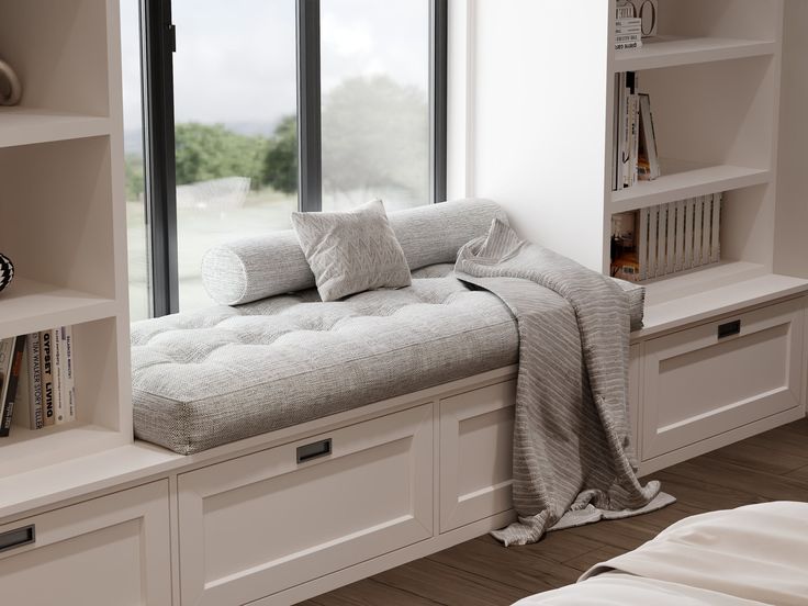 a white couch sitting in front of a window next to a book shelf filled with books