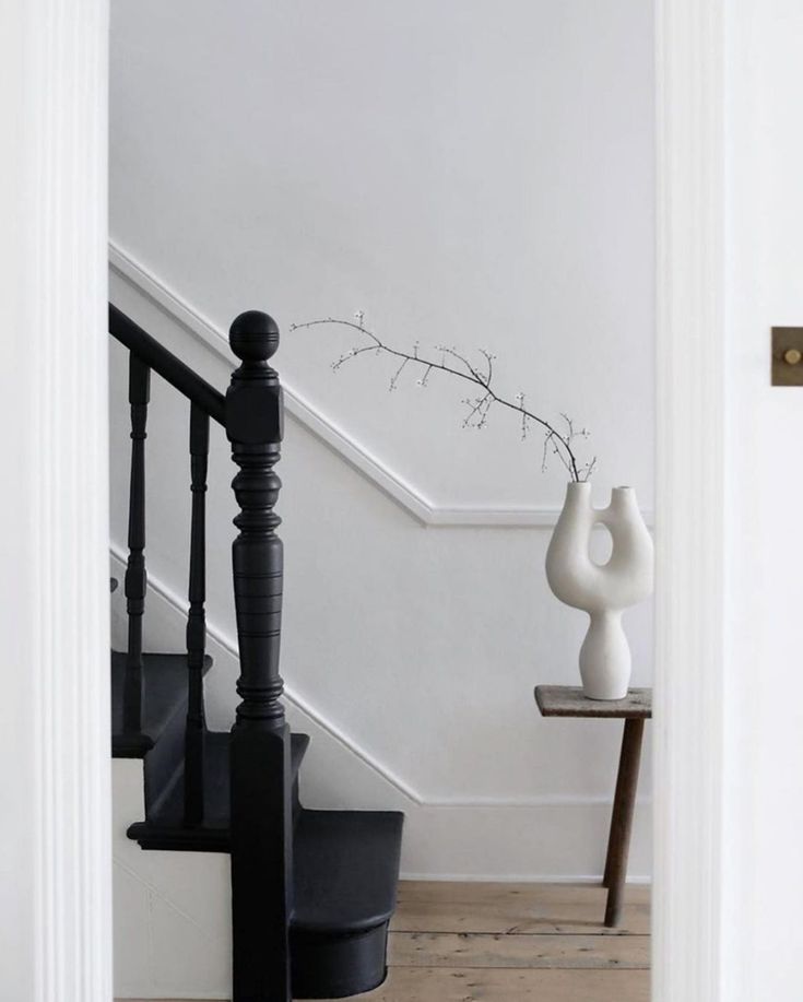 a white vase sitting on top of a wooden floor next to a stair case and railing