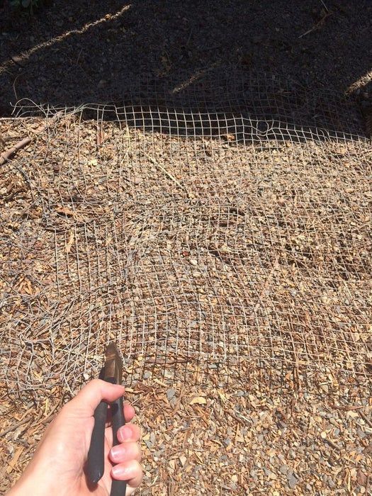 a person holding a tool in front of a wire mesh fence on top of dry grass