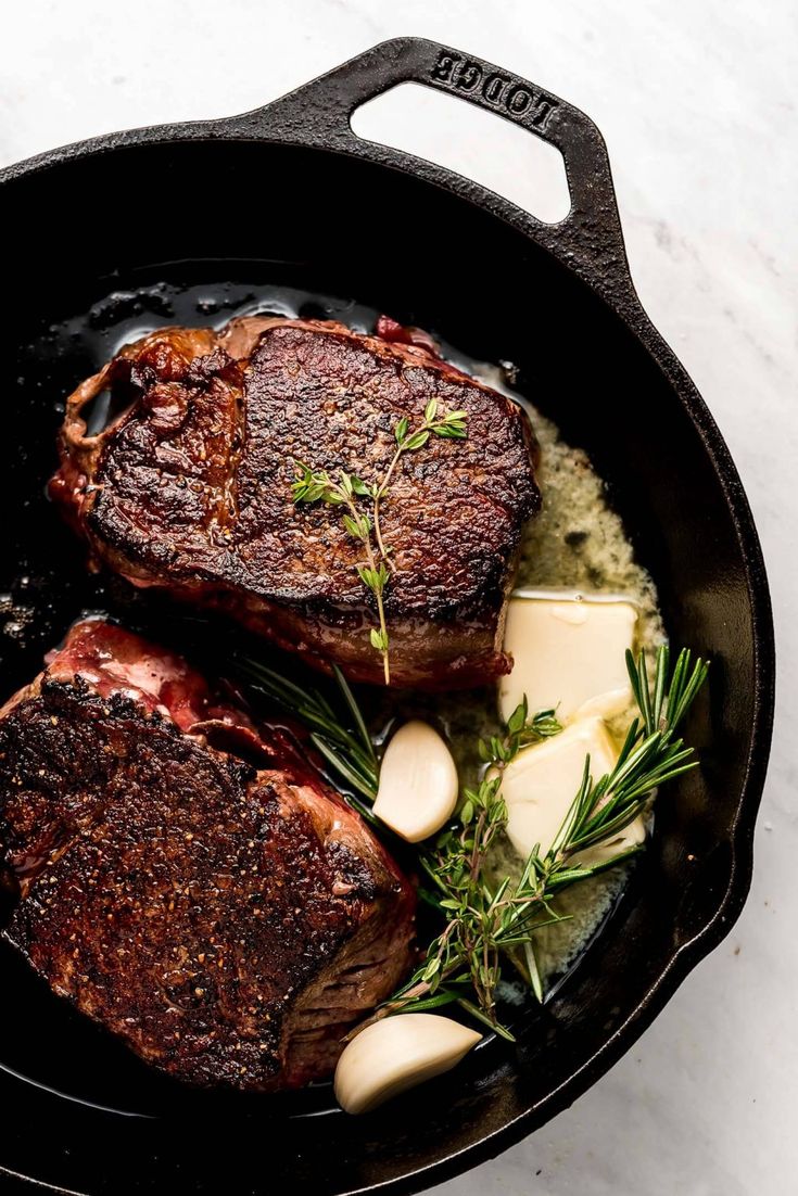 two steaks in a skillet with potatoes and herbs