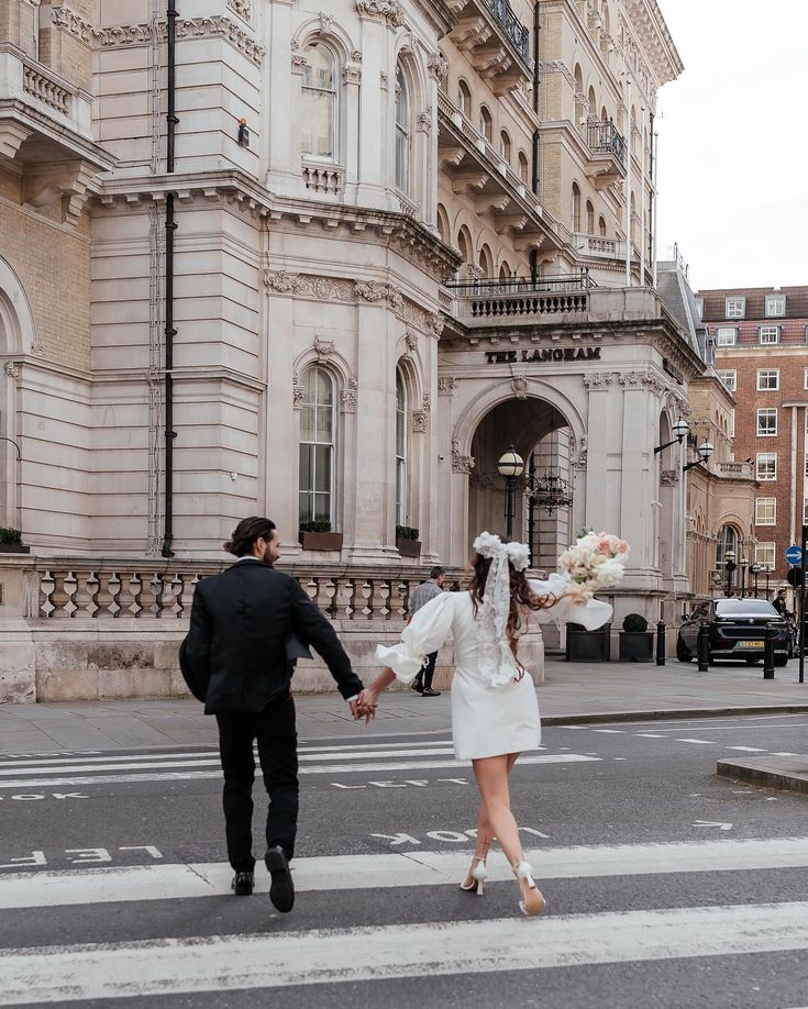 a bride and groom crossing the street in front of an old building