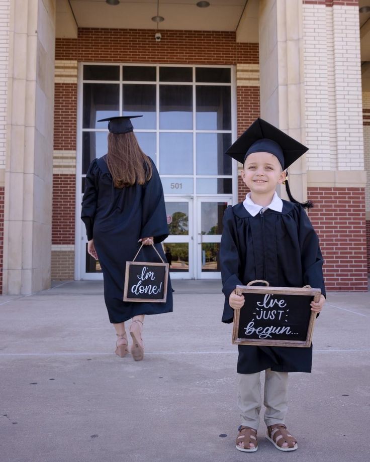 two children in graduation gowns holding signs