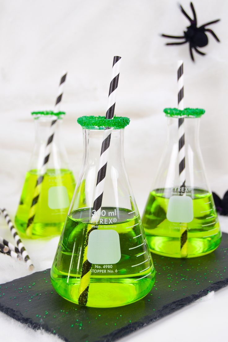 three beakles filled with green liquid and black and white straws sitting on top of a table