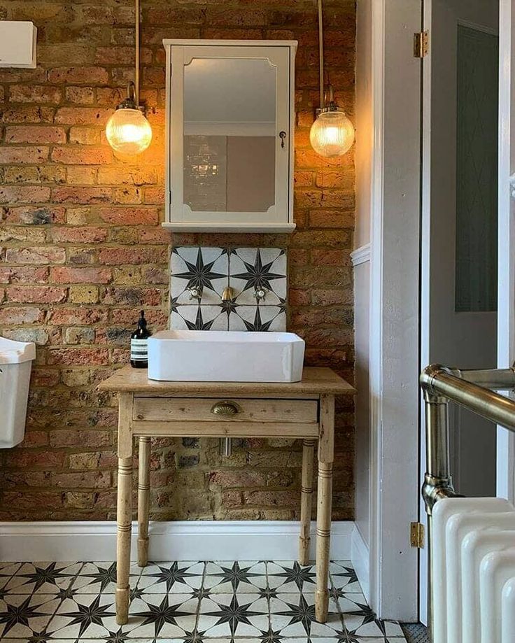 a bathroom with a sink and mirror next to a radiator in front of a brick wall