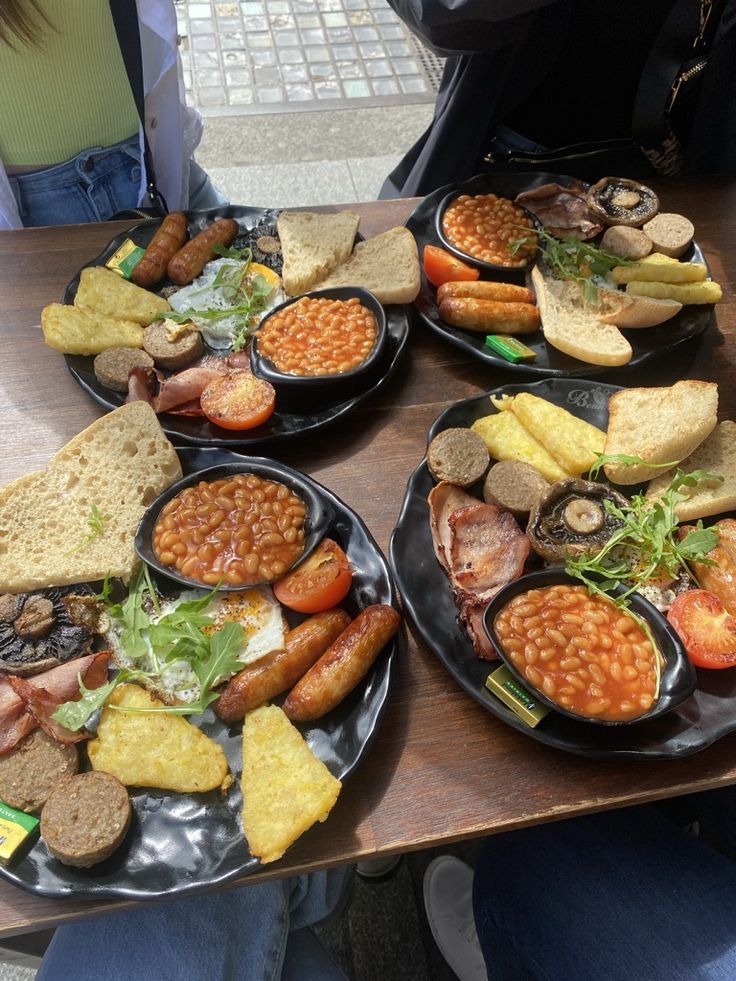 a table topped with black plates filled with different types of food and bread on top of it