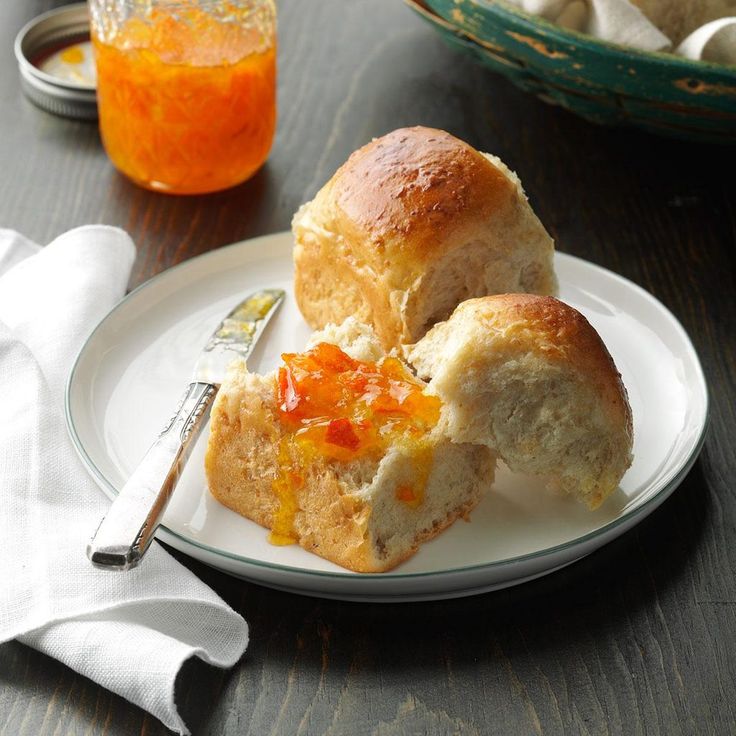 two rolls on a white plate next to a glass of orange juice and silverware