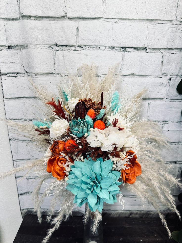 a vase filled with flowers and feathers on top of a wooden table next to a brick wall