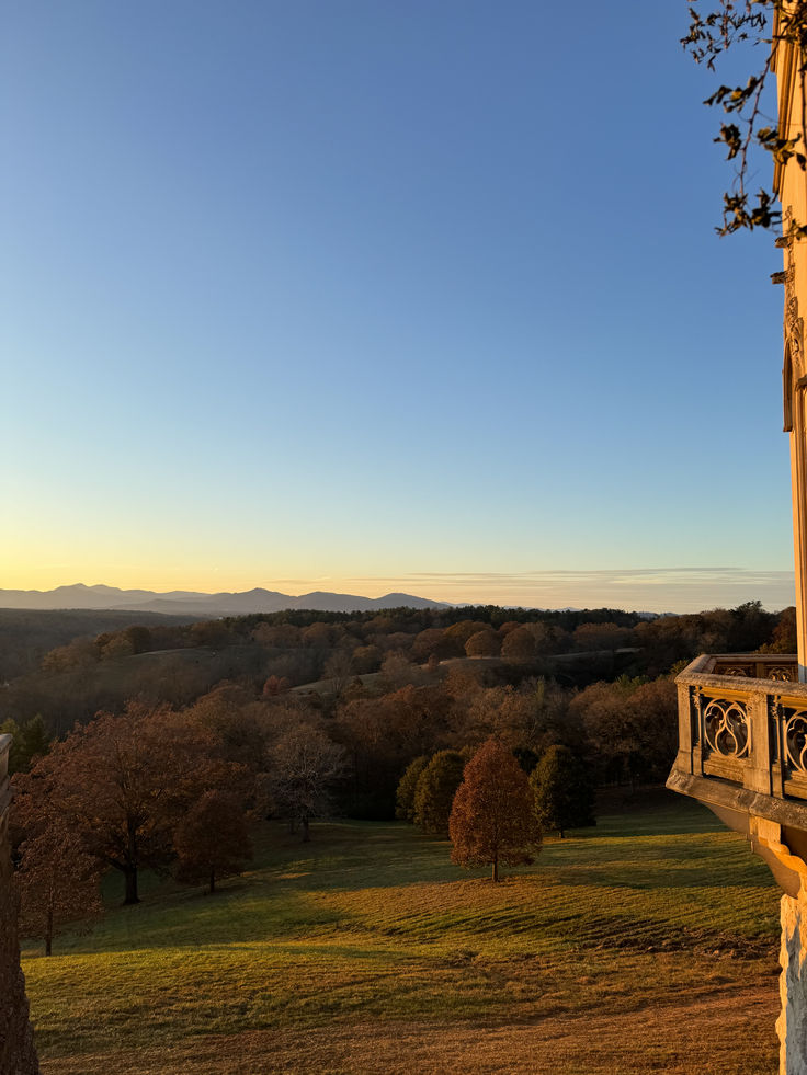 the sun is setting over an open field with trees and hills in the distance,