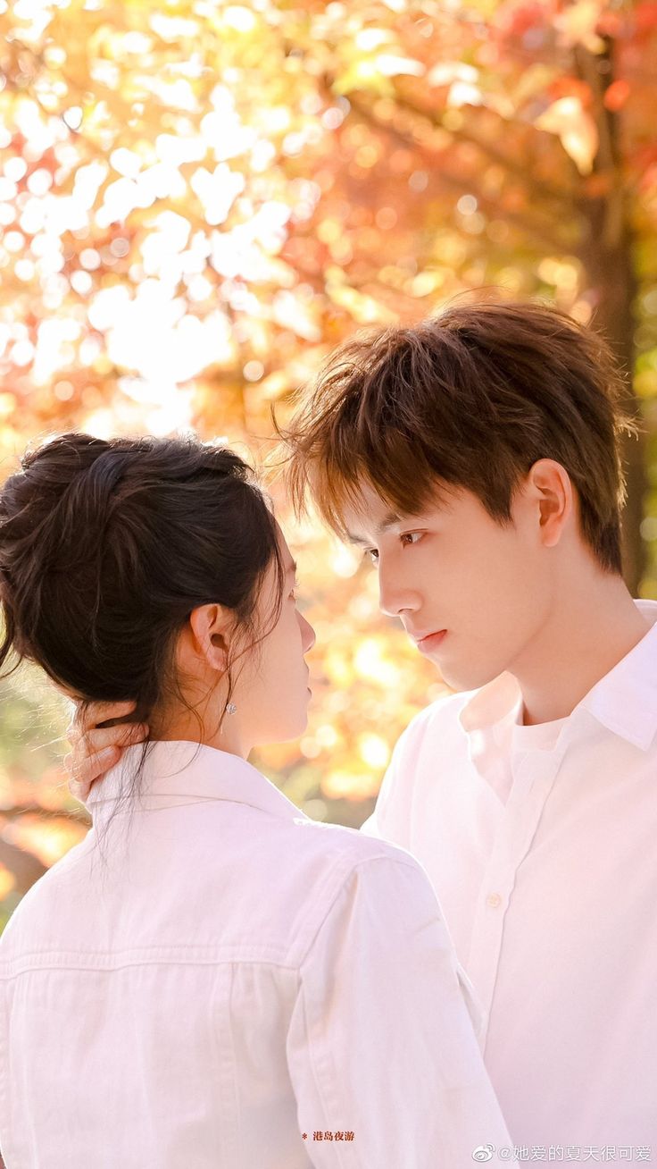 two young people standing next to each other in front of trees with leaves on them