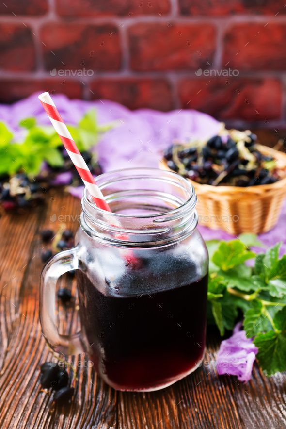 a glass mug filled with black liquid next to some green leaves and purple flowers on a wooden table