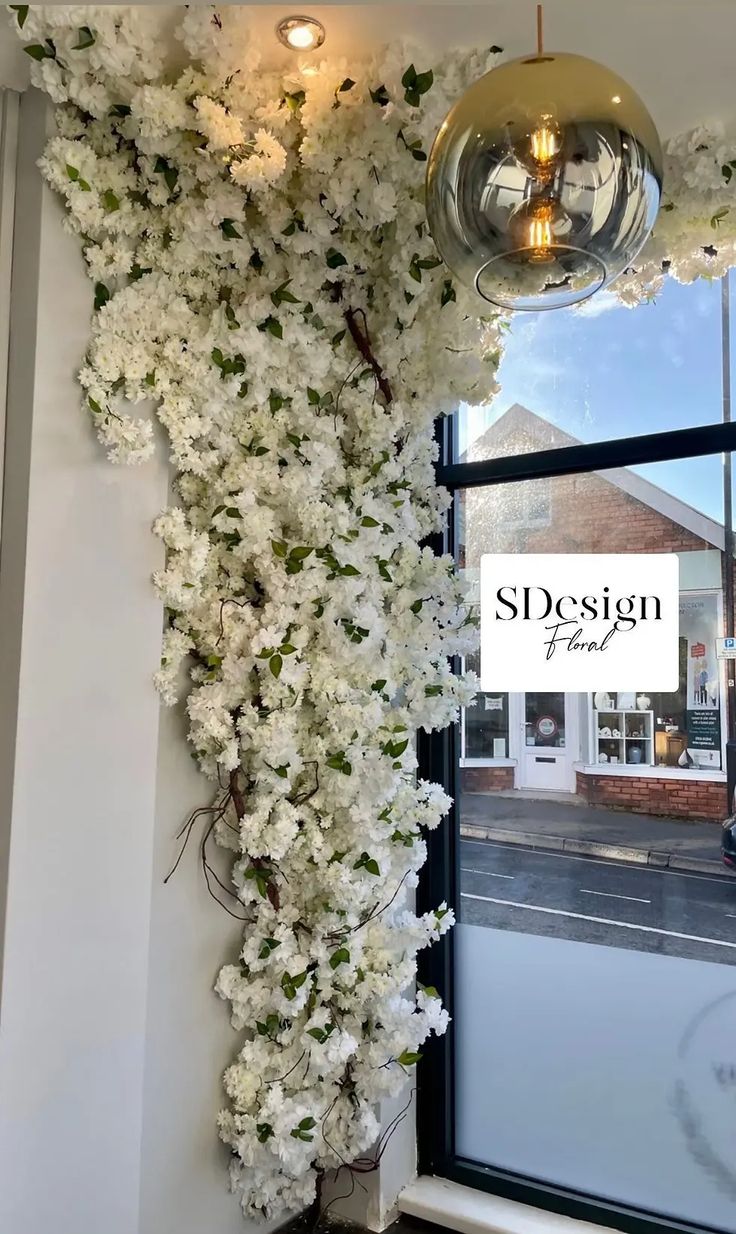 white flowers are growing up the side of a window in front of a storefront