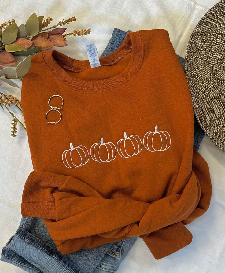 Cool Fall days and Pumpkin Patches, that's what we love!  The days become shorter but they sure seem to slow down.  Our simple pumpkin outline crew in the beautiful burnt orange is the perfect way to show you love the season in perfect minimalist style.  You will stay cozy and warm while looking super cute!   Pair with your favorite jeans, or size up one and grab your comfy leggings!  Features: 50% USA cotton, 50% polyester Pill-resistant air jet yarn Made with 50% sustainably and fairly grown U Pumpkin Sweatshirt Diy, Fall Graphic Sweatshirt, Pumpkin Embroidery Designs, Fall Embroidery Designs Sweatshirt, Cute Fall Sweatshirts, Embroidered Halloween Sweatshirt, Fall Embroidered Sweatshirts, Embroidery Designs Clothes, Fall Sweatshirt Ideas