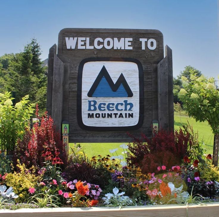 the welcome sign to beech mountain is surrounded by colorful flowers and greenery on a sunny day