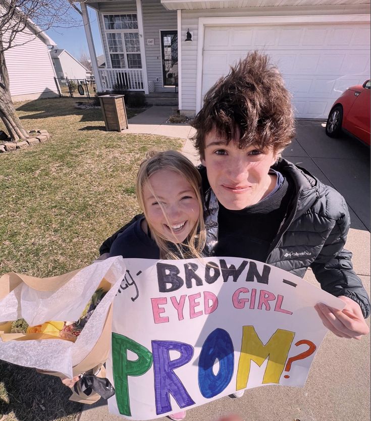 a boy and girl holding up a sign that says, brown eyed girl prom?