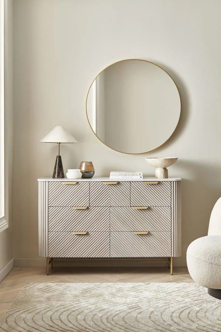 a white and gold dresser with a round mirror above it